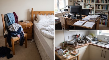 Una silla con ropa, una cama desordenada, una mesita de noche con cables, un escritorio con computadora y papeles, y una cocina con platos sucios y recipientes.