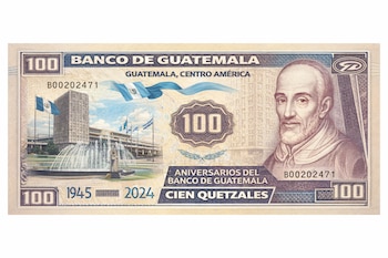 Primer plano de un billete conmemorativo de 100 Quetzales de Guatemala. Muestra la sede del Banco de Guatemala con una fuente y banderas, y el retrato de un hombre barbudo.