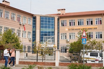 Edificio de tres pisos con letrero en turco, canasta de baloncesto en el patio, dos hombres caminando afuera y señales de tránsito