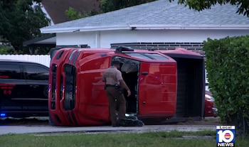 Un SUV Land Rover Range Rover Sport rojo está volcado en una calle, con un oficial de policía de pie junto a él y vidrios rotos en el suelo