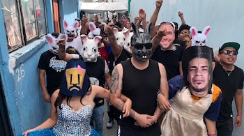 Personas con máscaras de conejos blancos y negros, vestidos formales y máscaras faciales caminan levantando los puños en un pasillo azul.