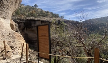 Vista de la Cueva de las Ventanas en Cuarenta Casas, Chihuahua, con un sendero de madera y un cartel informativo, rodeada de formaciones rocosas y vegetación