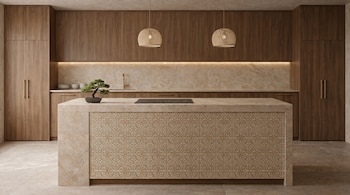 Cocina moderna con gabinetes de madera y encimeras de mármol. Isla central con estufa, bonsái y paneles decorativos. Iluminación bajo gabinetes y dos lámparas colgantes.