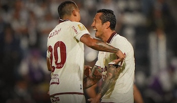 Dos futbolistas con la camiseta crema de Universitario de Deportes se abrazan en el campo de juego