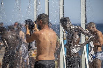 Varios jóvenes migrantes se duchan en una playa de Ceuta. (Marcos Moreno / Europa Press)