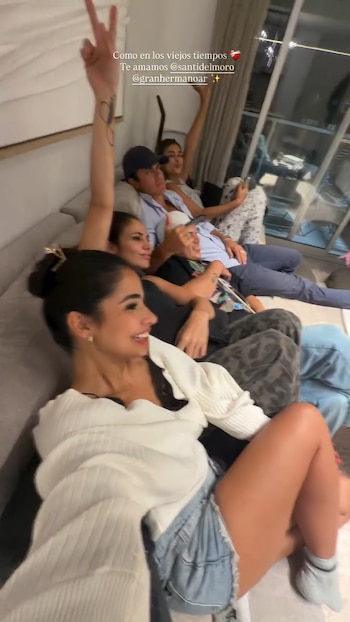 Seis ex participantes de Gran Hermano se sientan en un sofá en un interior, sonriendo y charlando. Una mujer en primer plano lleva una blusa blanca y shorts de jean