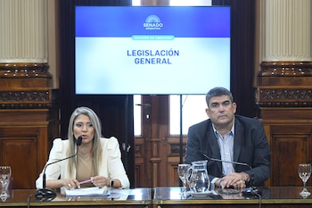 Una mujer rubia con saco blanco habla por un micrófono frente a un hombre. Detrás, una pantalla muestra "Senado Argentina" y "Legislación General"