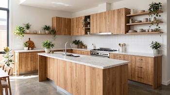Cocina con isla central de madera y mesada blanca, gabinetes superiores, estufas de acero y plantas de interior en macetas sobre los estantes.