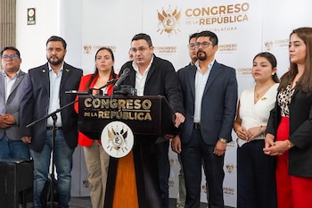 Grupo de siete personas, cinco hombres y dos mujeres, frente a un podio con el logo y nombre 'Congreso de la República'. Un hombre central habla al micrófono