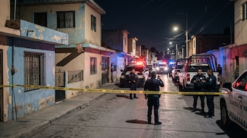 Agentes de seguridad y patrullas estacionadas en una calle de noche detrás de una cinta amarilla con la leyenda Precaución no pase.