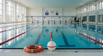 Vista frontal de una piscina olímpica cubierta con carriles delimitados, líneas de seguridad y salvavidas en los costados, en un entorno luminoso y moderno.