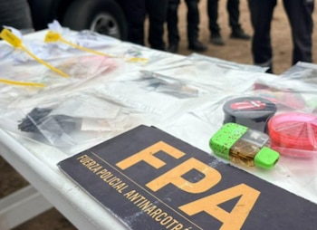 Una mesa blanca exhibe bolsas plásticas con etiquetas amarillas, molinillos y un cartel de la Fuerza Policial Antinarcotráfico