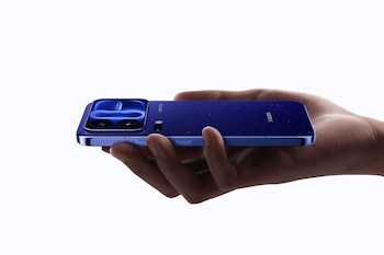 Mano que sostiene de perfil un teléfono inteligente azul marca Xiaomi con módulo de cámaras Leica sobre un fondo blanco