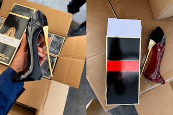 Frascos de perfume en forma de zapato de tacón alto en color negro y rojo junto a cajas de cartón y empaques.