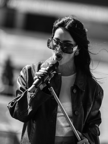 Fotografía en blanco y negro de Lali Espósito cantando con micrófono, gafas de sol y chaqueta de cuero