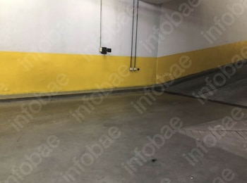 Un espacio interior con suelo de concreto gris y paredes blancas que presentan una franja horizontal amarilla en su parte inferior, con conductos eléctricos
