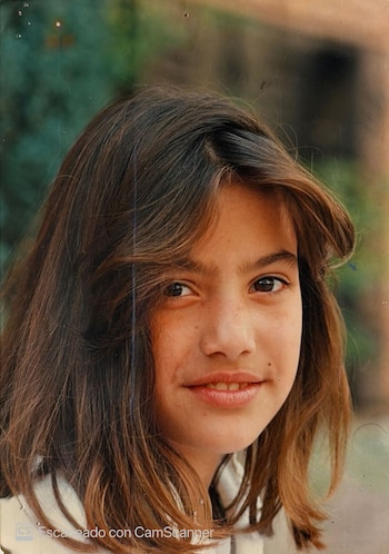 Primer plano del rostro de una niña con cabello castaño largo y ojos oscuros frente a un fondo desenfocado