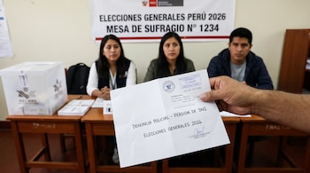 Primer plano de una mano sosteniendo una denuncia policial de pérdida de DNI frente a una mesa de votación con tres miembros de mesa y un cartel de Elecciones Perú 2026.