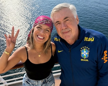 Carlo Ancelotti con chaqueta deportiva azul de Brasil posa junto a una mujer con pañuelo rosa en la cubierta de un barco sobre el mar