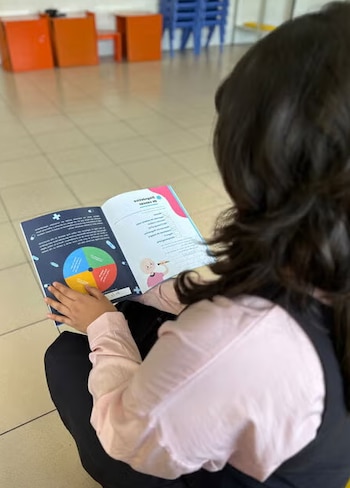 Camila explora las páginas interactivas de La Maleta de Emely, la herramienta que le permitió ponerle nombre, color y comprensión a su diagnóstico de leucemia en El Salvador (Cortesía OPS).