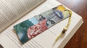 Un marcapáginas con recortes de un gato, peces, una medusa y un sol descansa sobre las hojas de un libro abierto.