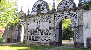Gran portón de piedra decorado con mosaicos negros y blancos, con dos arcos y puertas abiertas. Árboles verdes a los lados y al fondo