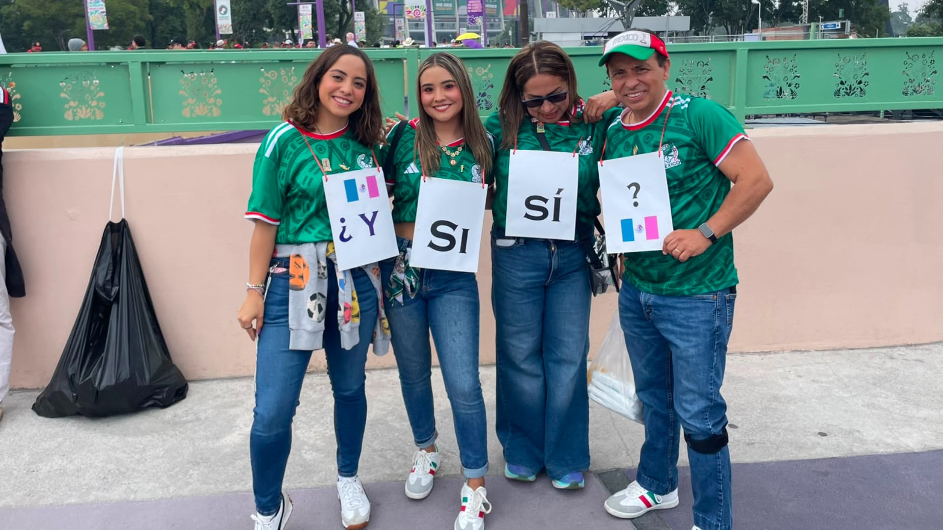 Cuatro aficionados con camisetas de México sostienen carteles individuales que forman la frase ‘¿Y Sí, Sí?’ en un evento deportivo. (Luis Mote | Infobae México)