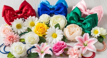 Tres lazos de pelo grandes en rojo, azul y verde, y gomas de pelo con flores artificiales de margaritas, rosas y lirios de varios colores.
