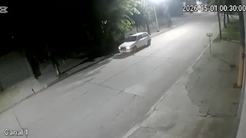 Imagen de CCTV nocturna mostrando un coche blanco circulando por una calle iluminada con farolas en Lobería, con árboles y edificios al fondo
