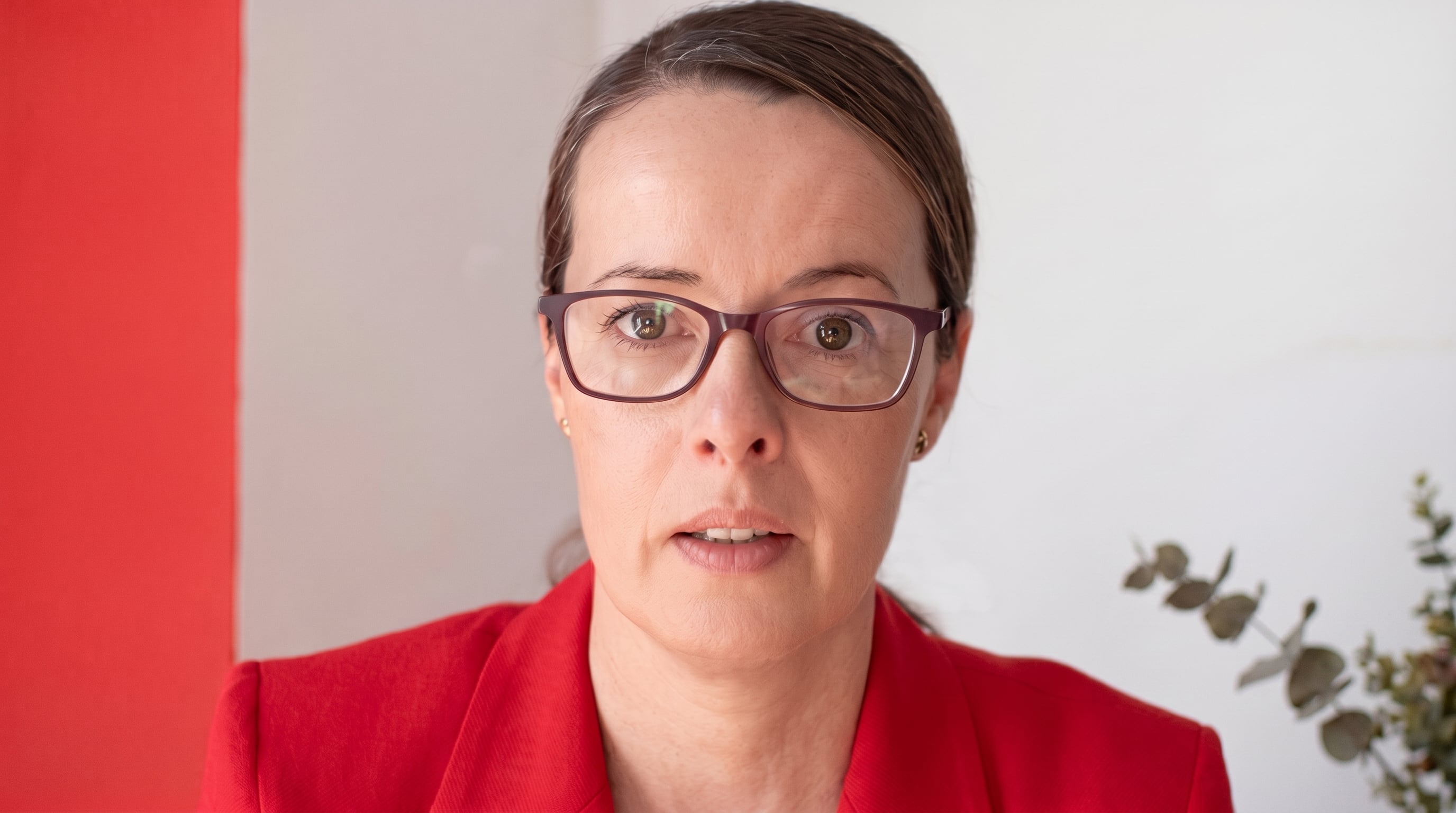 Una mujer con gafas de marco oscuro y chaqueta roja mira fijamente hacia la cámara. (Imagen Ilustrativa Infobae)