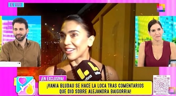 Vania Bludau sonríe durante una entrevista con micrófono de Latina TV; en segundo plano, dos presentadores de televisión y un banner en pantalla