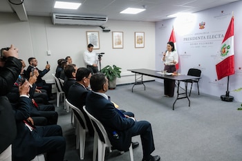Mujer hablando en micrófono, mesa negra, hombres sentados, bandera de Perú, letrero "Oficina de la Presidenta Electa Keiko Fujimori 2026-2031", cámara