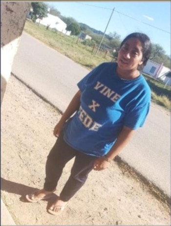 Una mujer con camiseta azul, pantalón negro y sandalias está de pie en un camino de tierra