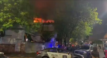 Vehículos de la policía en una calle de noche frente a un edificio que presenta llamas y humo en el piso superior