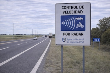 Señal de tráfico blanca con texto "Control de Velocidad por Radar" de la Agencia Nacional de Seguridad Vial en Ruta Nacional 3, con autos en la vía y cielo nublado.