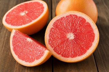 Dos mitades de pomelo, un gajo y un pomelo entero sobre una mesa de madera.