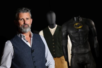 El fundador y director ejecutivo de Propstore, Stephen Lane, posa cerca del Batitraje dañado en batalla, usado por Michael Keaton en Batman, y el traje de Jack Dawson, usado por Leonardo DiCaprio en Titanic (Reuters)