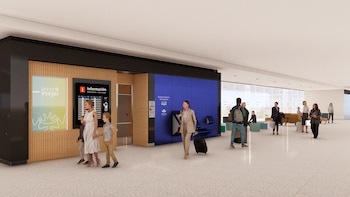 Vista interior de un moderno terminal de aeropuerto con varias personas, pantallas de información, una pared de listones de madera y piso claro