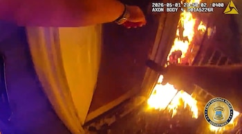 Imagen de cámara corporal: un brazo se extiende hacia una puerta con intensas llamas naranjas saliendo del interior de un edificio. Se ve el logo de Chattanooga Police