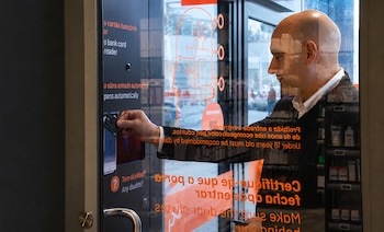 Hombre inserta tarjeta en lector de puerta de cristal. La puerta tiene texto y gráficos. Se observan reflejos del interior y exterior