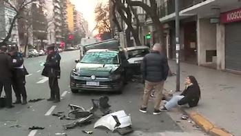 Un automóvil negro dañado en una calle con restos de partes plásticas en el suelo, policías y una persona sentada en la acera