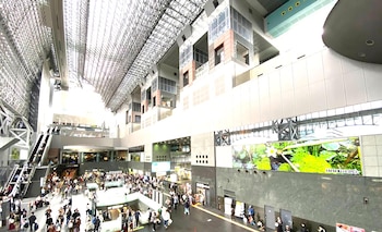 Interior de la Estación de Kioto con un techo reticular de metal y vidrio. Múltiples niveles, escaleras mecánicas y una multitud de personas en movimiento