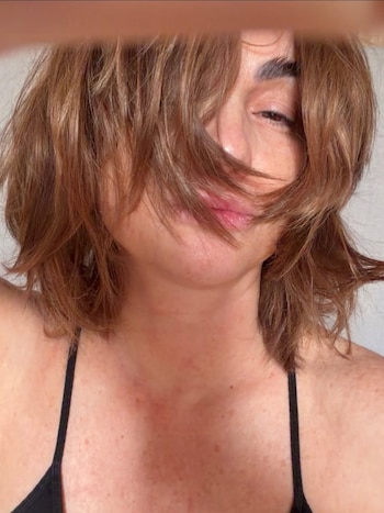 Primer plano de Araceli González. Su cabello castaño desordenado cubre parcialmente su rostro. Un ojo está entrecerrado y los labios ligeramente abiertos. Viste un top negro de tirantes