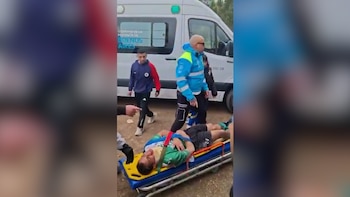 Hombre con camiseta verde en camilla azul y amarilla. Personal médico y un hombre de azul cerca. Ambulancia blanca con texto Buenos Aires