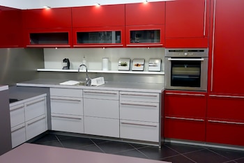 Cocina moderna con gabinetes superiores rojos, gabinetes inferiores blancos, encimera gris, fregadero cromado, horno empotrado de acero inoxidable