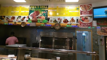 Interior de un restaurante de comida rápida con un empleado en la cocina, un gran menú en la pared y una vitrina con hornos de cocina