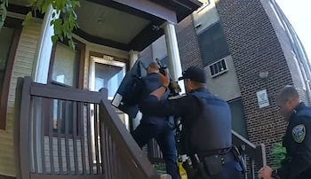 Tres agentes de policía con equipo táctico y un escudo balístico ascienden por la escalera de entrada a una residencia