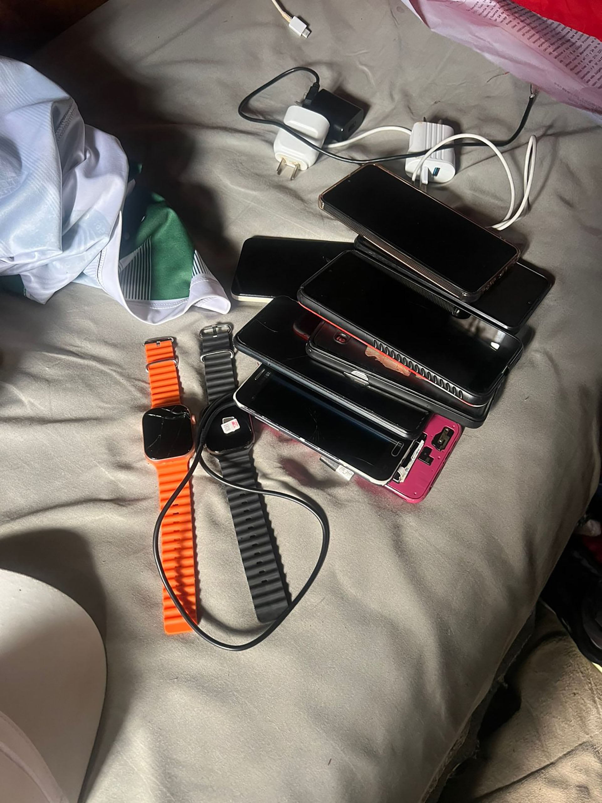 Celulares y relojes inteligentes junto a cargadores y cables, se encuentran sobre una tela gris incautados en la prisión