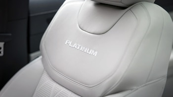 Asiento de vehículo en cuero de color claro con la palabra 'PLATINUM' en relieve, costuras y un patrón de perforaciones