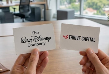 Primer plano de dos manos sosteniendo tarjetas blancas con los logotipos de The Walt Disney Company y Thrive Capital, sobre un fondo de oficina desenfocado
